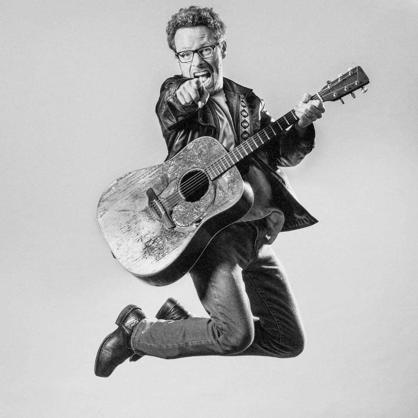 photo of musician Brad Thompson holding guitar jumping in the air